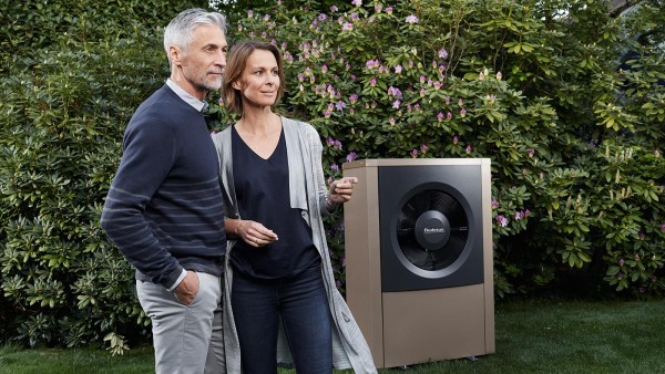 couple debout dans le jardin à côté d'une pompe à chaleur