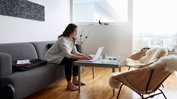 Mladá žena pracujúca z domu na laptope, sediac za stolom v obývacej izbe