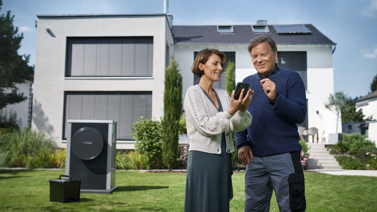 Žena s montážnikom stojaca pred moderným domom s fotovoltikou a tepelným čerpadlom